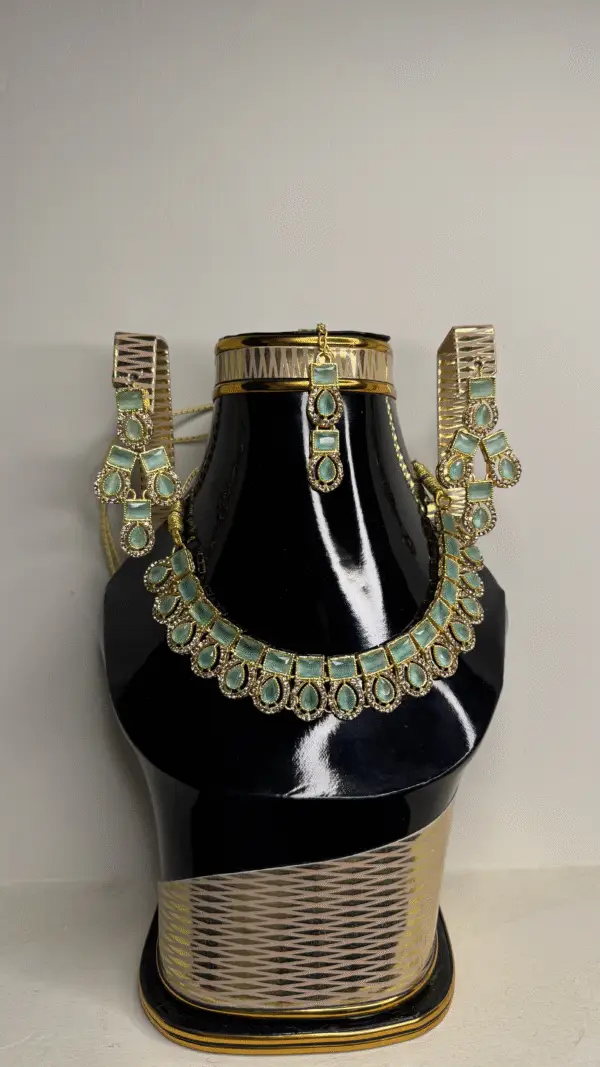 A gold necklace set with matching earrings and a choker, featuring green gemstones, displayed on a black mannequin bust.