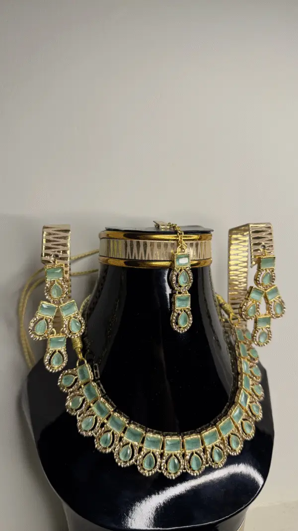 A Zircon gold necklace set with matching earrings and a choker, featuring green gemstones, displayed on a black mannequin bust.